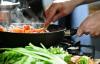 Hands, light complexion, stirring food in a pan on a stove.