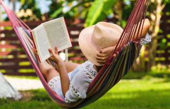 person in a straw hat, reading a book while relaxing in a hammock