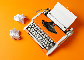 A typewriter and crumpled paper balls. Paper in the typewriter says "Chapter 1"